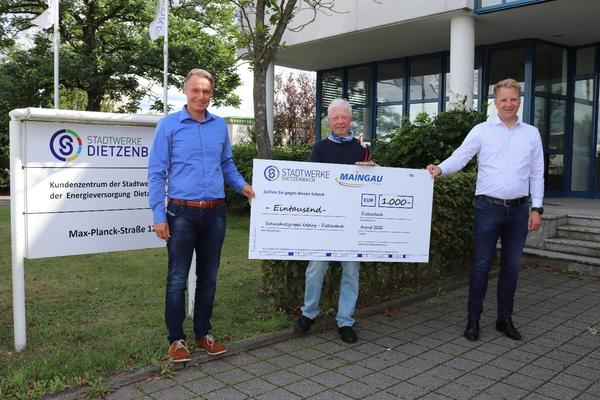 Bild vergr&ouml;&szlig;ern: Thomas Vollmuth, Gesch&auml;ftsf&uuml;hrer der Stadtwerke Dietzenbach (links), &uuml;berreicht gemeinsam mit MAINGAU-Vertriebsleiter Dominik Habig (rechts) den Scheck an Rudolf Keim. Einen geh&auml;kelten Storch gab's auch gleich noch dazu.   